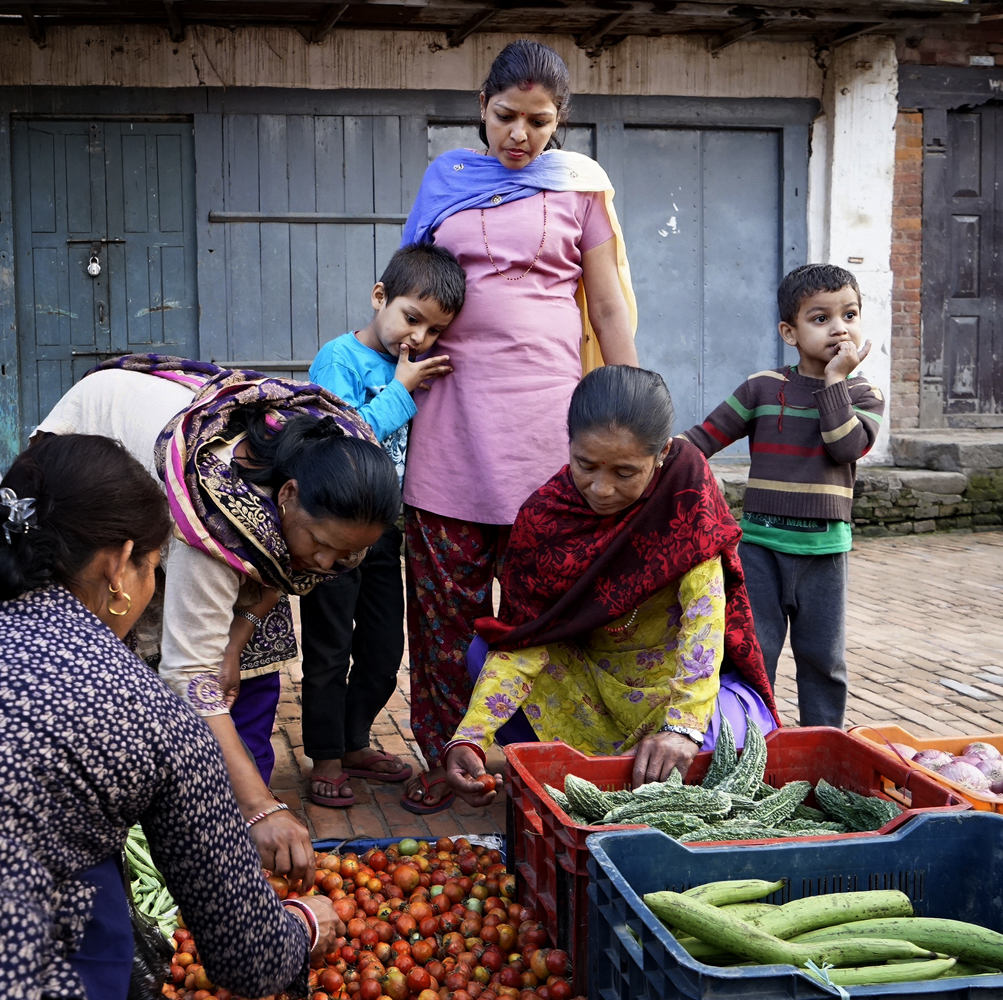 Street photography, food, nepalese women, children, boys, bored, colorful clothing,  scarf, costume, tomatoes, cucumbers, vegetables, shopping, choosing, Bhaktapur, Nepal
