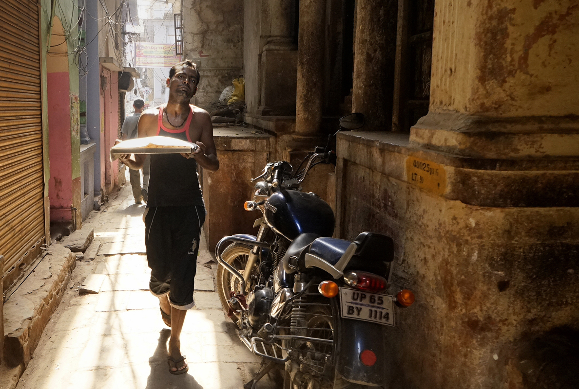 Street photography, food, motorbike, ancient alleyway, narrow passage, stone buildings, man with food tray, Varanasi, India