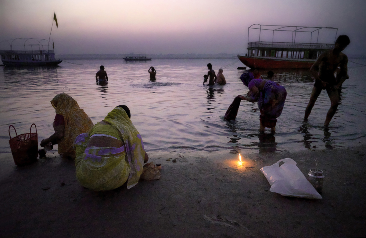Street photography, morning ritual, observance, candle, people bathing, river, women washing, river, boats, dawn, Varanasi, India