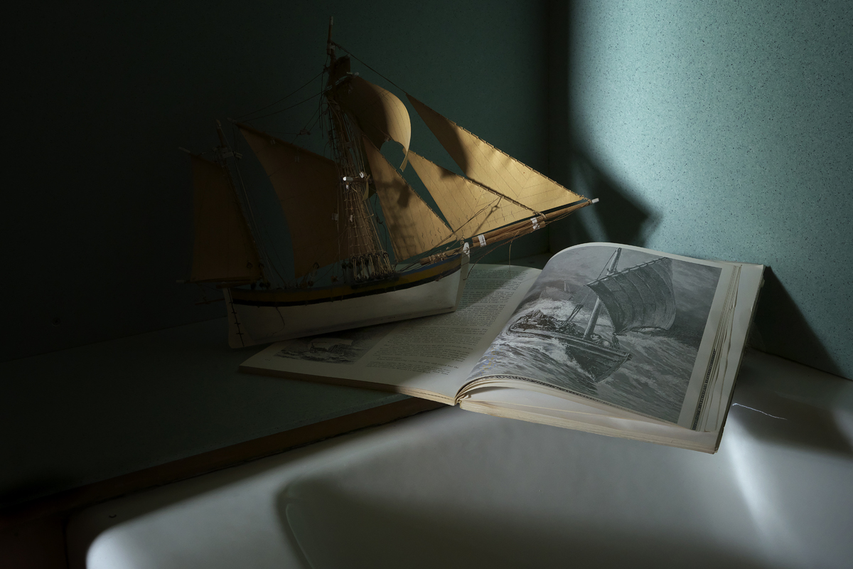 Nautical still life, bathtub, model ship, book, ship in storm etching