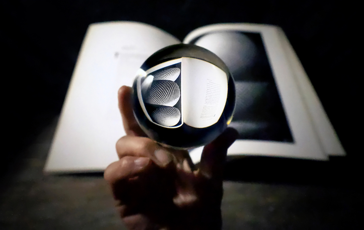 Still life, hand holding crystal ball, book on Escher art, art book