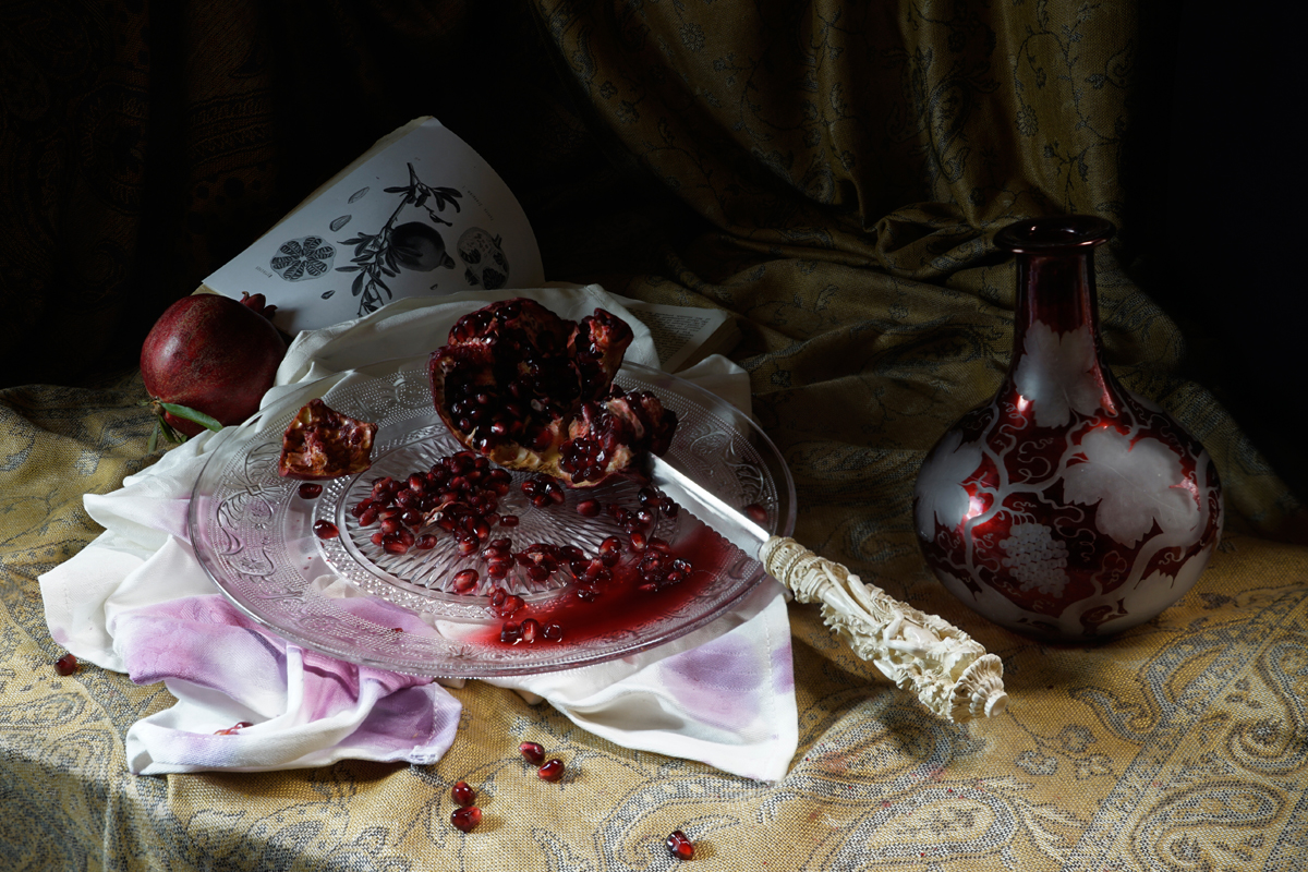 Food still life, pomegranate, juicy, cut fruit, knife, red glass vase, book